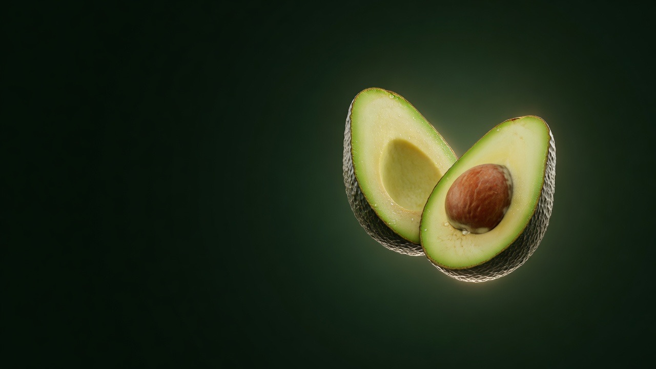 Palta Hass partida por la mitad, con su cuesco, flotando sobre fondo verde oscuro